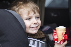 Adorable toddler boy with blue eyes in safety car seat eating sweet ice cream