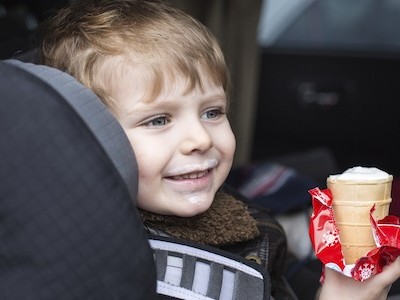 Adorable toddler boy with blue eyes in safety car seat eating sweet ice cream
