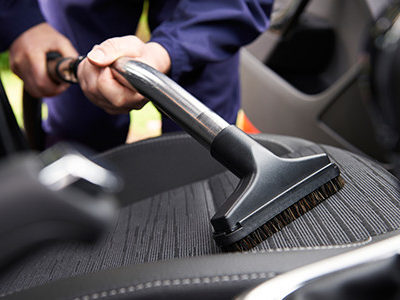 Person Cleaning Car Seats With Compressed Air And A Brush
