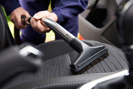 Person Cleaning Car Seats With Compressed Air And A Brush